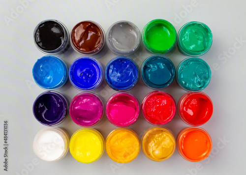 Open jars with gouache of different colors close-up on a gray background. Hobby - painting