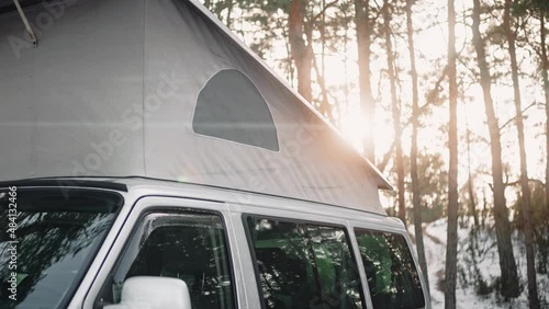 Close shot of camping van with pop up roof at the sunset in the woods in winter . Motorhome parked in a perfect camping spot in rays of sun. High quality 4k footage