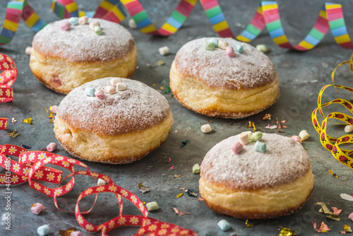 Krapfen, Berliner or donuts with streamers, confetti and mini marshmallows on gray background. Colorful carnival or birthday image