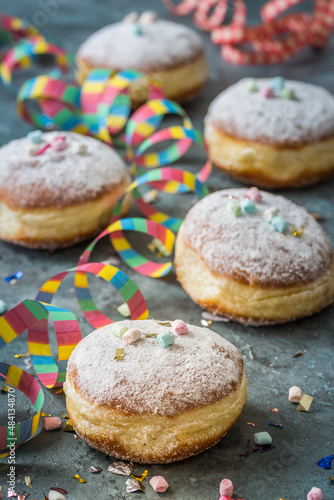 Krapfen, Berliner or donuts with streamers, confetti and mini marshmallows on gray background. Colorful carnival or birthday image, vertical