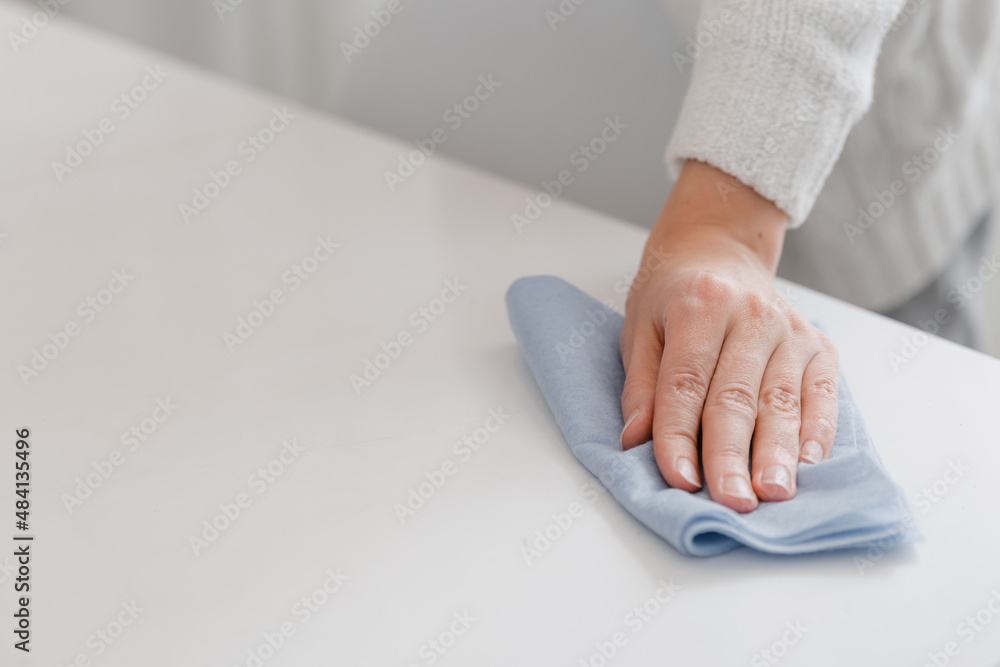 Fototapeta premium Cleaning the table with a blue microfiber cloth. Sanitize surfaces prevention in hospital and public spaces against coronavirus. Woman hand using wet wipe at home. Cleaning the room.
