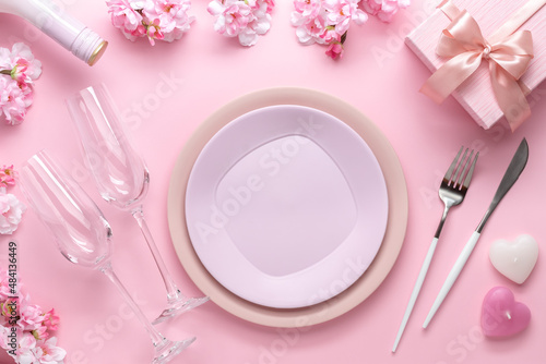 Place setting for Valentine's Day. Romantic dinner, table setting with cutlery. Pink background. Dating concept, love. Spring flowers, empty plate, glasses, champagne, holiday gift box.