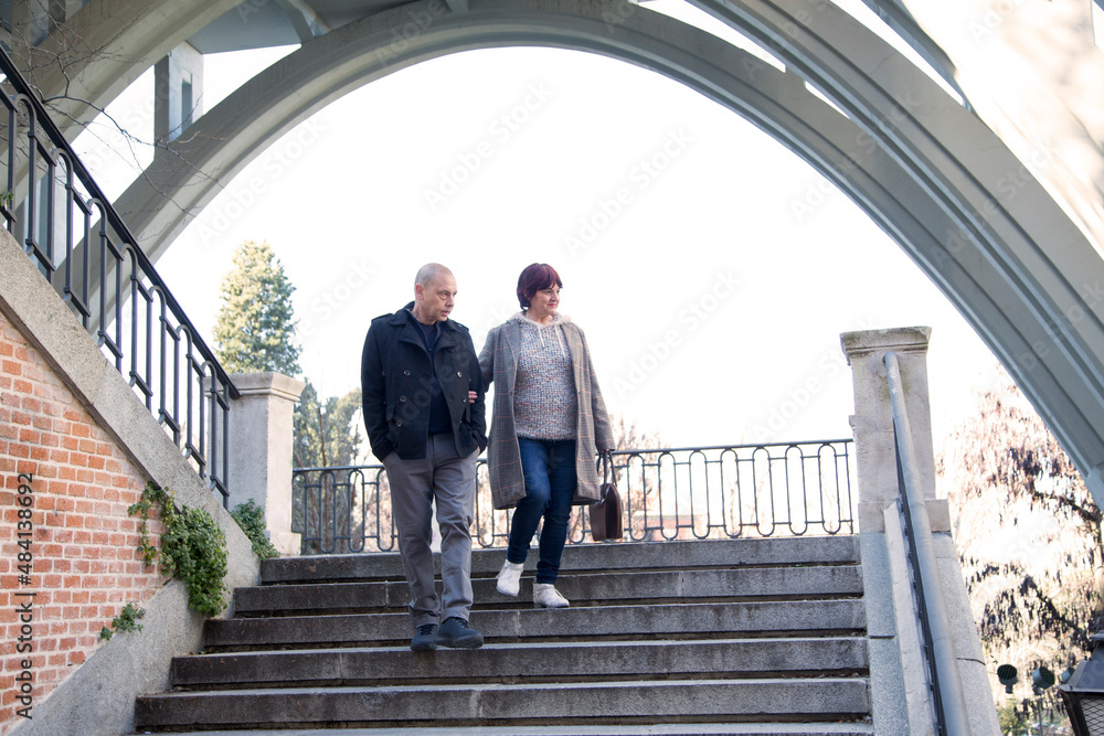 two elderly people holding hands walking down stairs in the city