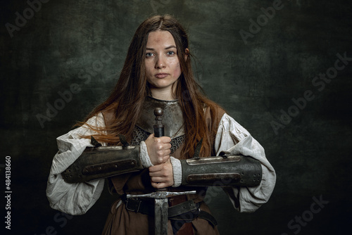 Obraz na płótnie Vintage portrait of adorable woman, medieval female warrior or knight with dirty wounded face looking at camera isolated over dark retro background