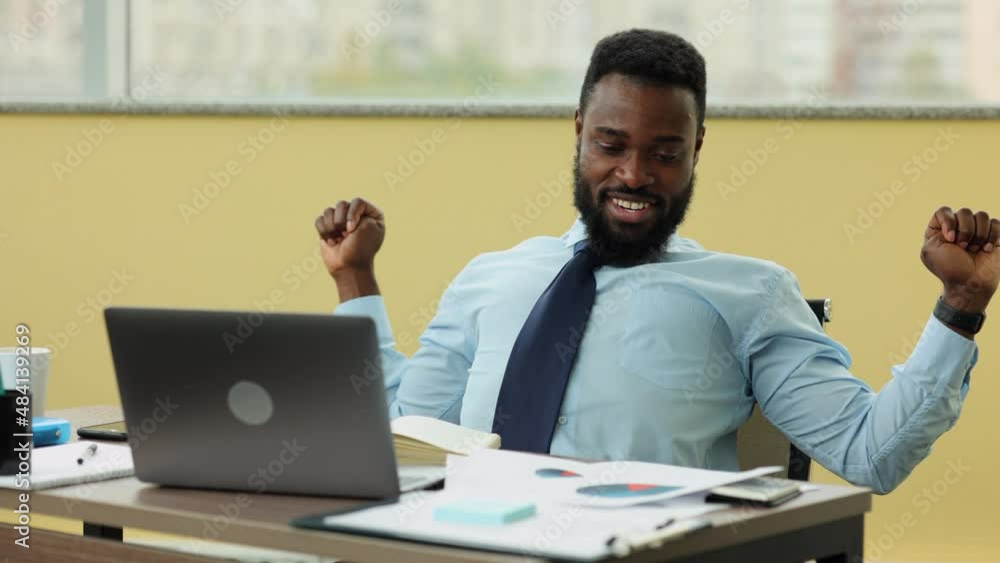 Young businessman or analyst having work break and sitting at table with laptop in office spbi. Closeup view of American African man rests and looks with smile, holds documents in hand and sits at Young businessman or analyst having work break and sitting at table with laptop in office spbi. Closeup view of American African man rests and looks with smile, holds documents in hand and sits at
