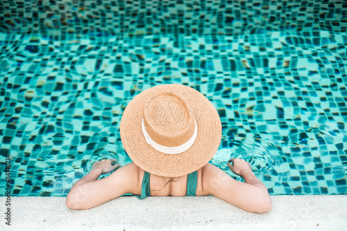 Happy woman in green swimsuit and hat in swimming pool at luxury hotel against ocean front. young female enjoy in tropical resort. Relaxing, summer,  travel, holiday, vacation and weekend concept