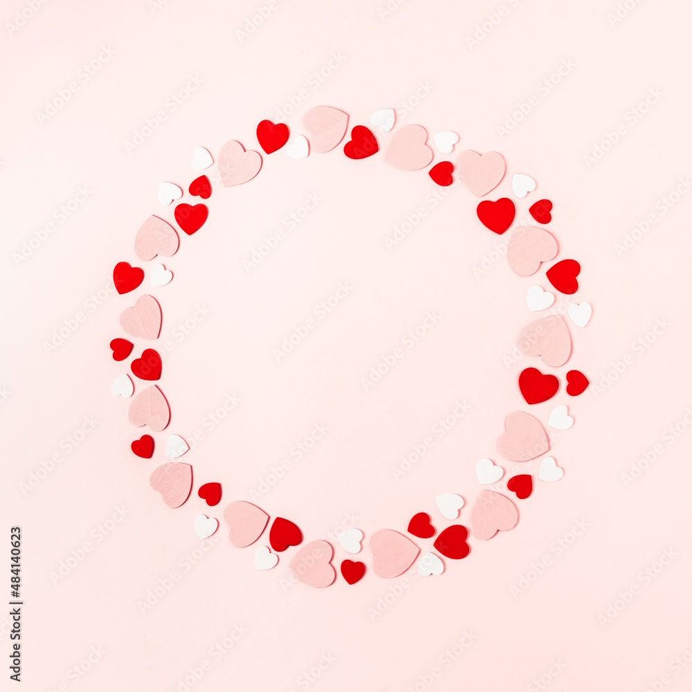 Round frame made of little red and white wooden hearts on pink background
