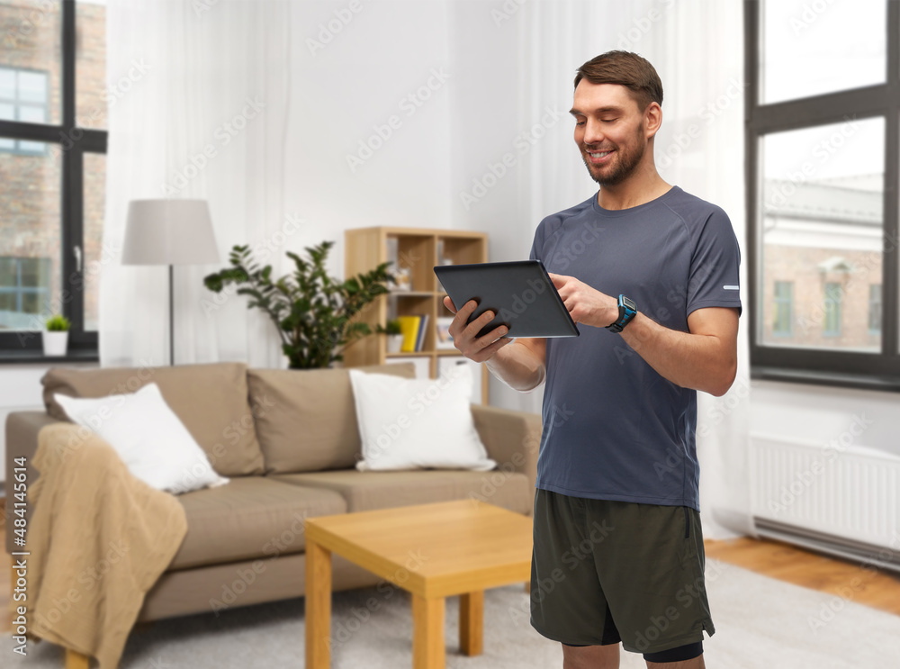 fitness, sport and healthy lifestyle concept - smiling man in sports clothes holding tablet pc computer over home room background fitness, sport and healthy lifestyle concept - smiling man in sports clothes holding tablet pc computer over home room background