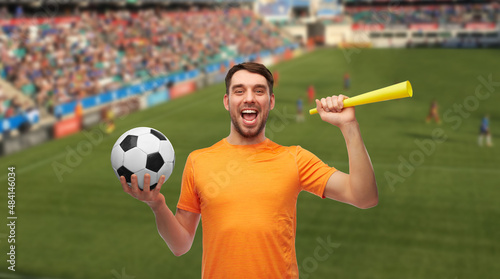 sport, leisure games and success concept - happy smiling man or football fan with soccer ball and vuvuzela over stadium background