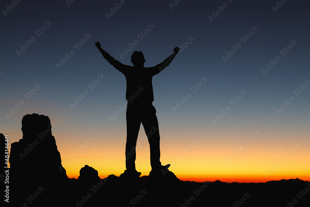 Successful people silhouette with open arms on rock morning sunset sky background.