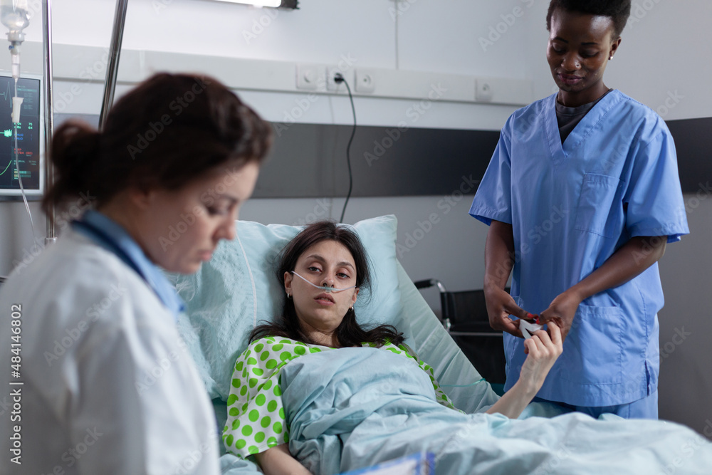 Nurse measuring spo2 saturation using pulse oximeter on patient finger while doctor is reading lab results in private ward. Woman attended on hospital bed with low oxygen saturation looking at medic. Nurse measuring spo2 saturation using pulse oximeter on patient finger while doctor is reading lab results in private ward. Woman attended on hospital bed with low oxygen saturation looking at medic.