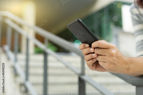Young woman wear a dress using modern smartphone device typing text message in social media while sitting on stairs outdoor. Happy female spending free time in break of working.