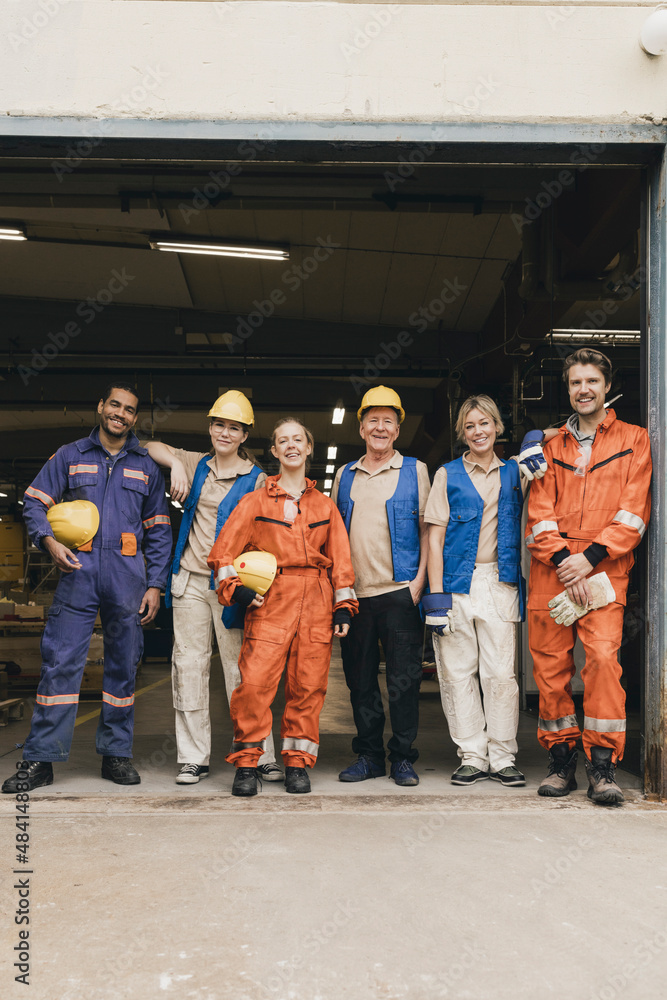 Smiling male and female blue-collar workers standing in factory warehouse Smiling male and female blue-collar workers standing in factory warehouse