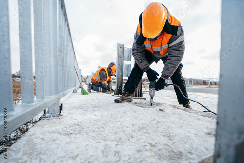 Road workers installing a new fence railing of bridge, outside the city 