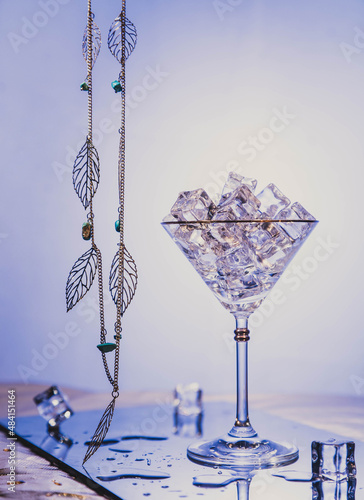 ice with martini and with ice. the glass stands on a transparent shiny table. transparent glass and shiny jewelry on a lilac background
