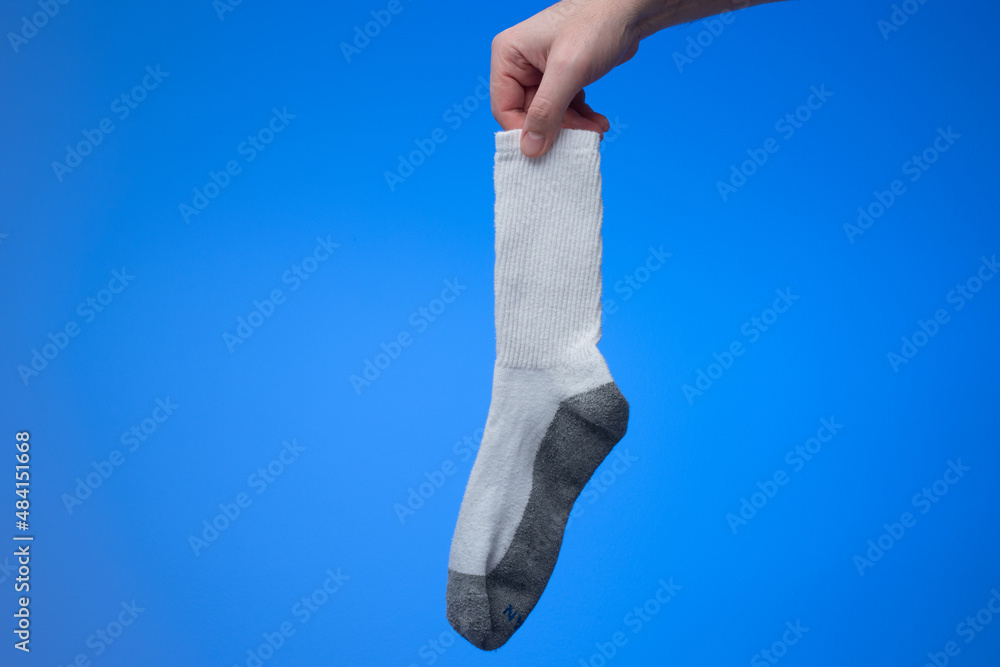Single dry and clean cotton sock held in hand by Caucasian male hand. Close up studio shot, isolated on blue background Single dry and clean cotton sock held in hand by Caucasian male hand. Close up studio shot, isolated on blue background