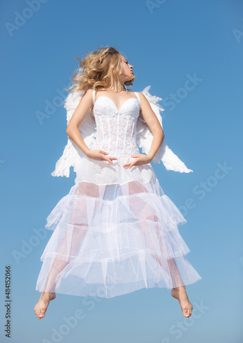 Valentines Day flying angel. Cupid girl with white wings. Woman with angel wings with bow and arrow against blue sky.