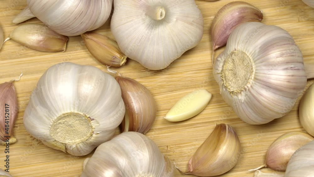 Fresh garlic bulbs and cloves on a wooden table, rotation background. Loop motion