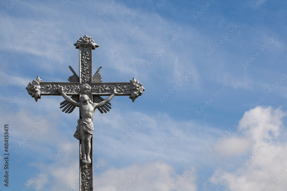 Cross from a roadside chapel against a blue sky with clouds.