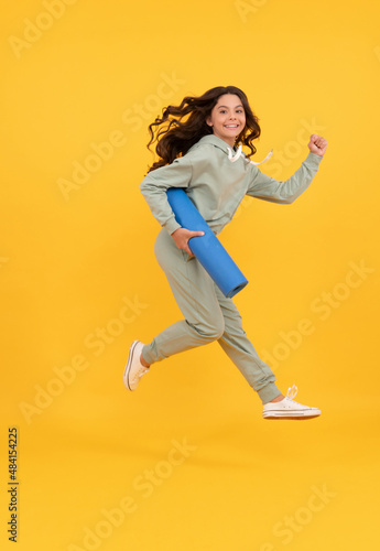 glad child in sportswear running with fitness mat. fit your body. sport teen girl training.