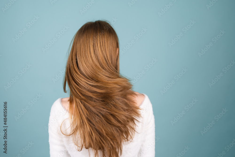 Close beauty portrait of a woman with perfect skin and natural makeup,white soft sweater, moving head shaking hair on a blue background