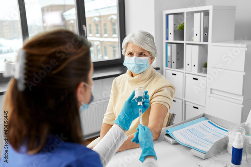 medicine, health and vaccination concept - doctor or nurse filling syringe with vaccine or drug and senior woman at hospital