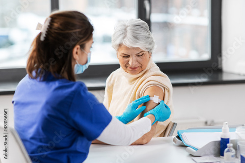 medicine, health and vaccination concept - doctor or nurse applying medical patch to vaccinated senior woman at hospital