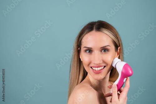 Close-up beauty portrait of topless woman with perfect skin and natural makeup  full nude lips  holding an electric facial brush. Facial cleansing with microvibrations.