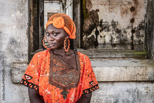 Принти на полотні Africa Woman in orange suit and headdress stands by an old building in Takoradi