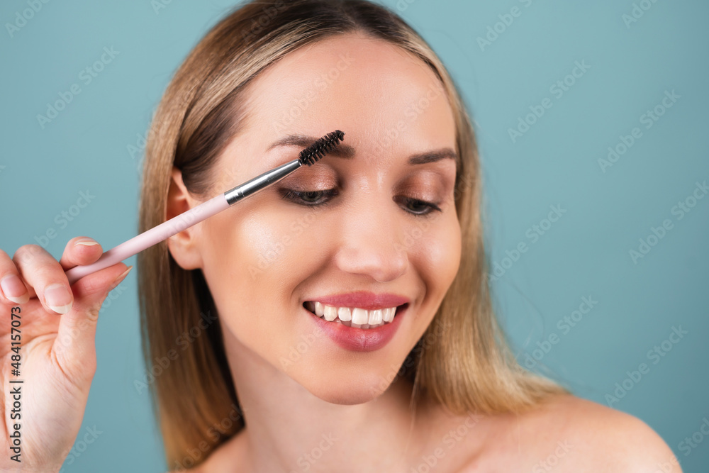 Close up beauty portrait of a woman with perfect skin and natural makeup, full nude lips, holding an eyebrow brush.