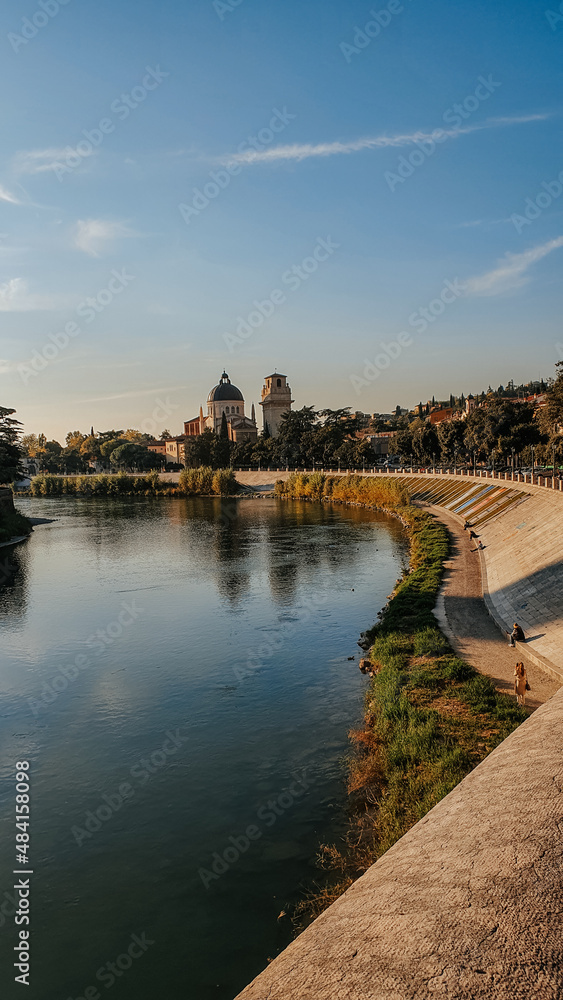 Photo taken over Ponte Pietra in Verona, Italy.  In the background there are houses, and a basilica on top of the mountain, with a blue sky and a bird flying.