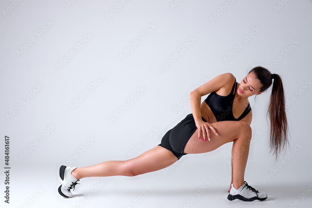 Fitness woman doing lunges exercises for leg muscle workout training, active athlete lady is doing front forward one leg step lunge exercise, on white studio background, side view