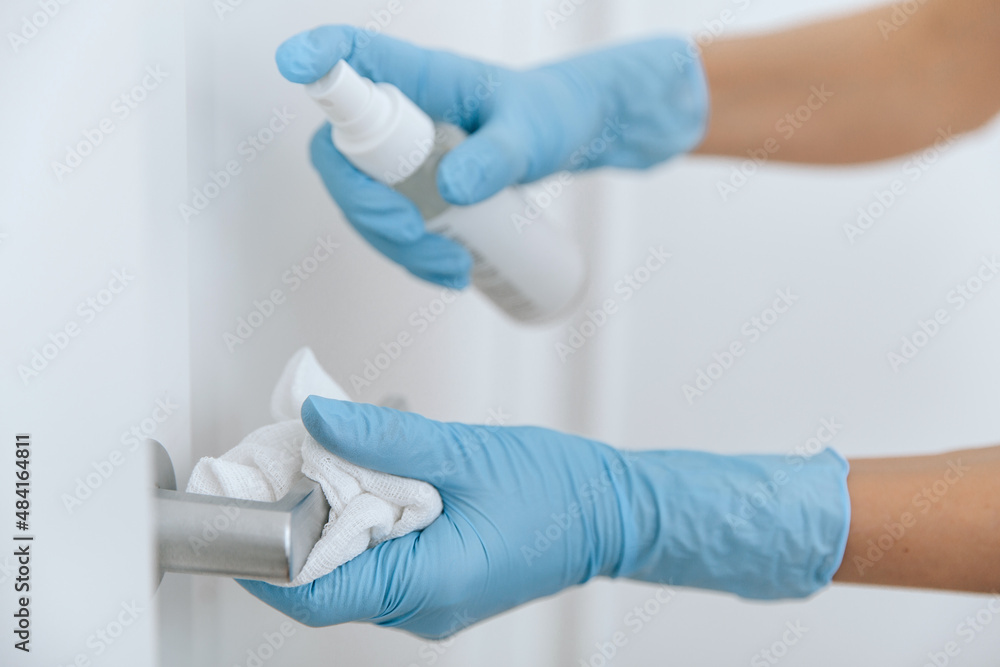 Cleaning black door handle with an antiseptic wet wipe, blue gloves and sanitizer. Woman hand using towel for cleaning. Sanitize surfaces prevention in hospital and public spaces against corona virus Cleaning black door handle with an antiseptic wet wipe, blue gloves and sanitizer. Woman hand using towel for cleaning. Sanitize surfaces prevention in hospital and public spaces against corona virus