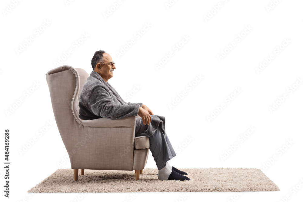 Profile shot of a mature man in a bathrobe sitting in an armchair - obrazy, fototapety, plakaty 
