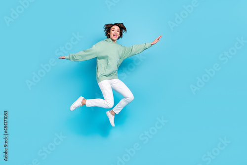 Full length photo of hooray young brunette lady jump wear hoodie pants shoes isolated on blue background © deagreez