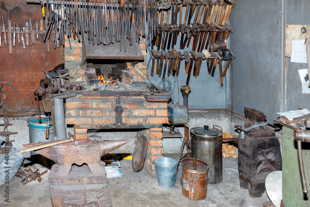 An old iron anvil against the background of the interior of a blacksmith shop with a brick oven.