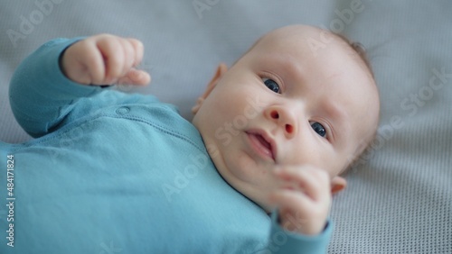 Cute two-month-old baby in blue clothes looks into camera. Sweet newborn boy lies on the sofa. Shooting from the upper angle of a chubby male kid. Beautiful infant boy with blue eyes.