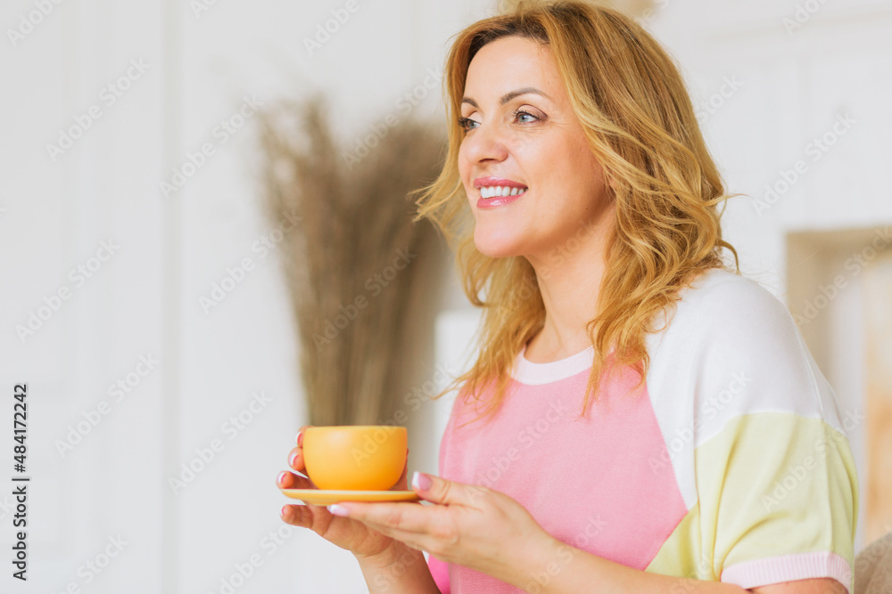 A beautiful mature woman in a pink sweater and yellow pants poses for the camera with a tea cup. A beautiful mature woman in a pink sweater and yellow pants poses for the camera with a tea cup.