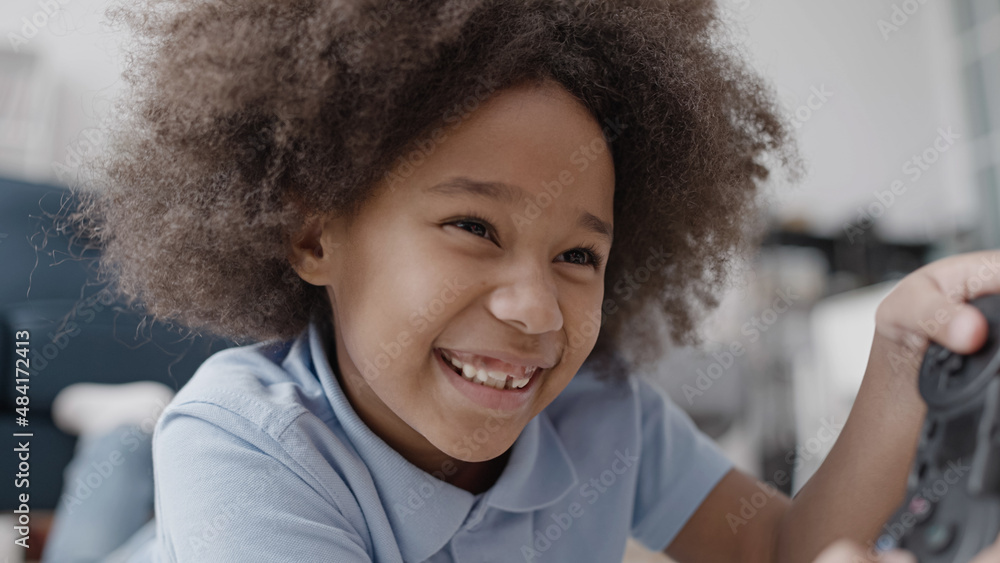 Positive little girl playing video game lying on the floor, smiling, showing missing tooth Positive little girl playing video game lying on the floor, smiling, showing missing tooth