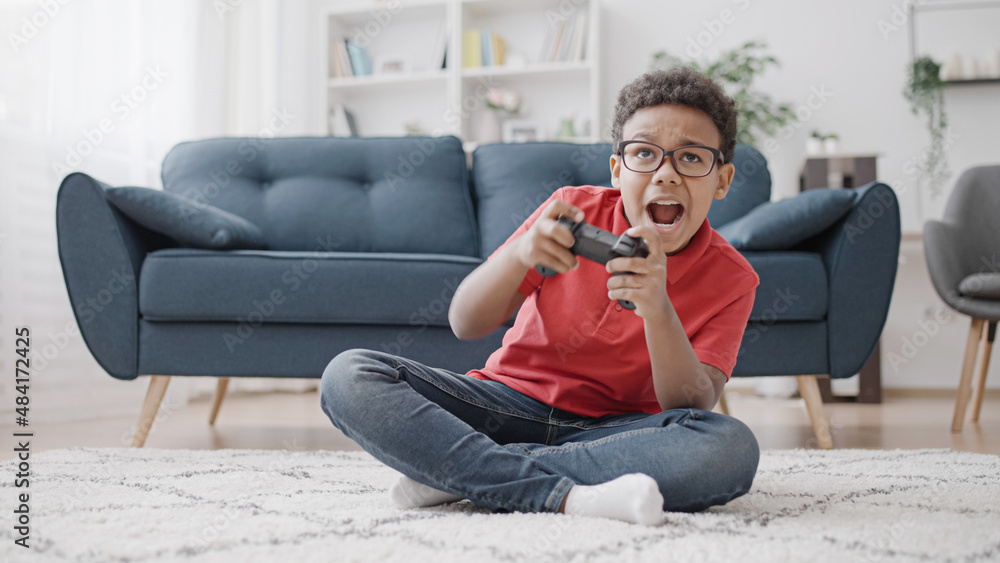 Excited African American boy playing video game with joystick controller at home