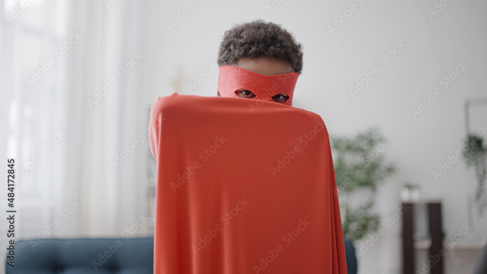 Little black boy hiding his face behind red cloak, pretending to be superhero Stock Photo