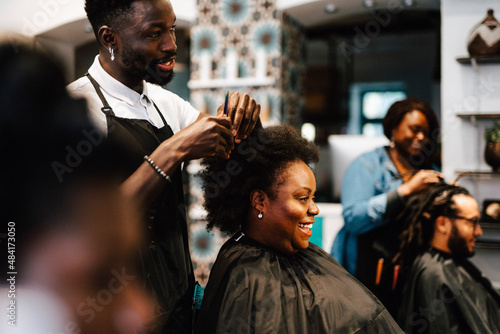 Male hairdresser cutting hair of smiling female customer at barber shop photo