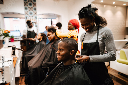 Smiling female barber making locs of male customer in salon photo