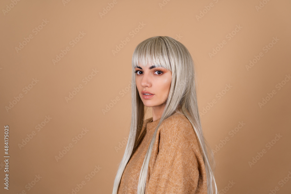 Blonde girl with bangs and brown daytime make-up in a sweater on beige background sensual fashion portrait Blonde girl with bangs and brown daytime make-up in a sweater on beige background sensual fashion portrait