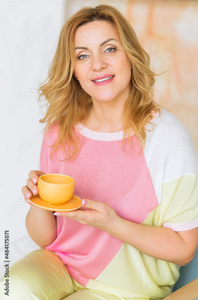 A beautiful mature woman in a pink sweater and yellow pants poses for the camera with a tea cup. A beautiful mature woman in a pink sweater and yellow pants poses for the camera with a tea cup.