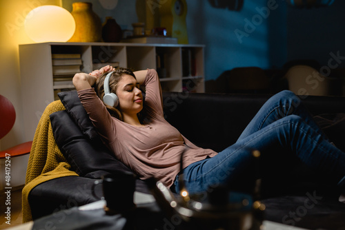 woman listening music on headphones and relaxing on sofa at home