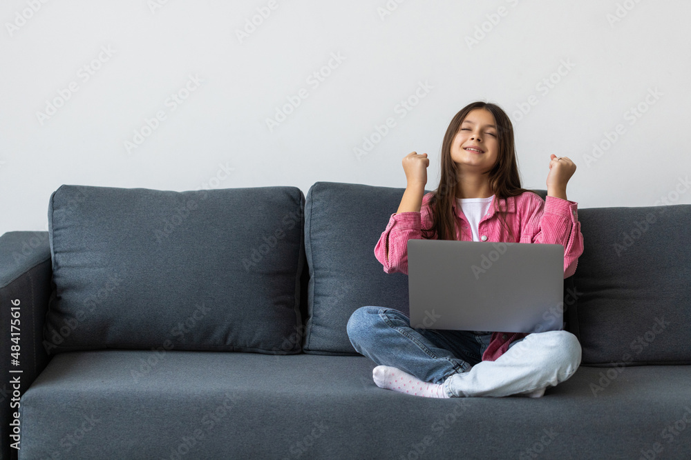 Portrait little girl sitting on couch talking on web camera passes test gesturing like winner Portrait little girl sitting on couch talking on web camera passes test gesturing like winner