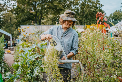 Man in hat watering plants in urban garden photo