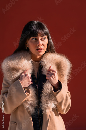 Posing of a brunette model in a winter jacket leaning against a wall with a bag. Caucasian pretty a red background