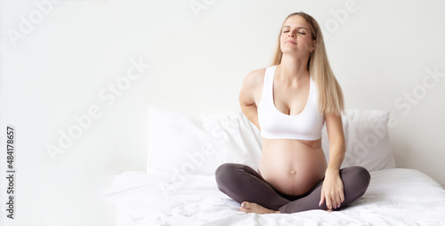 Beautiful blonde pregnant woman is sitting on the bed. Experiencing back pain. Problems bearing a child. Close-up. The background. Panarama